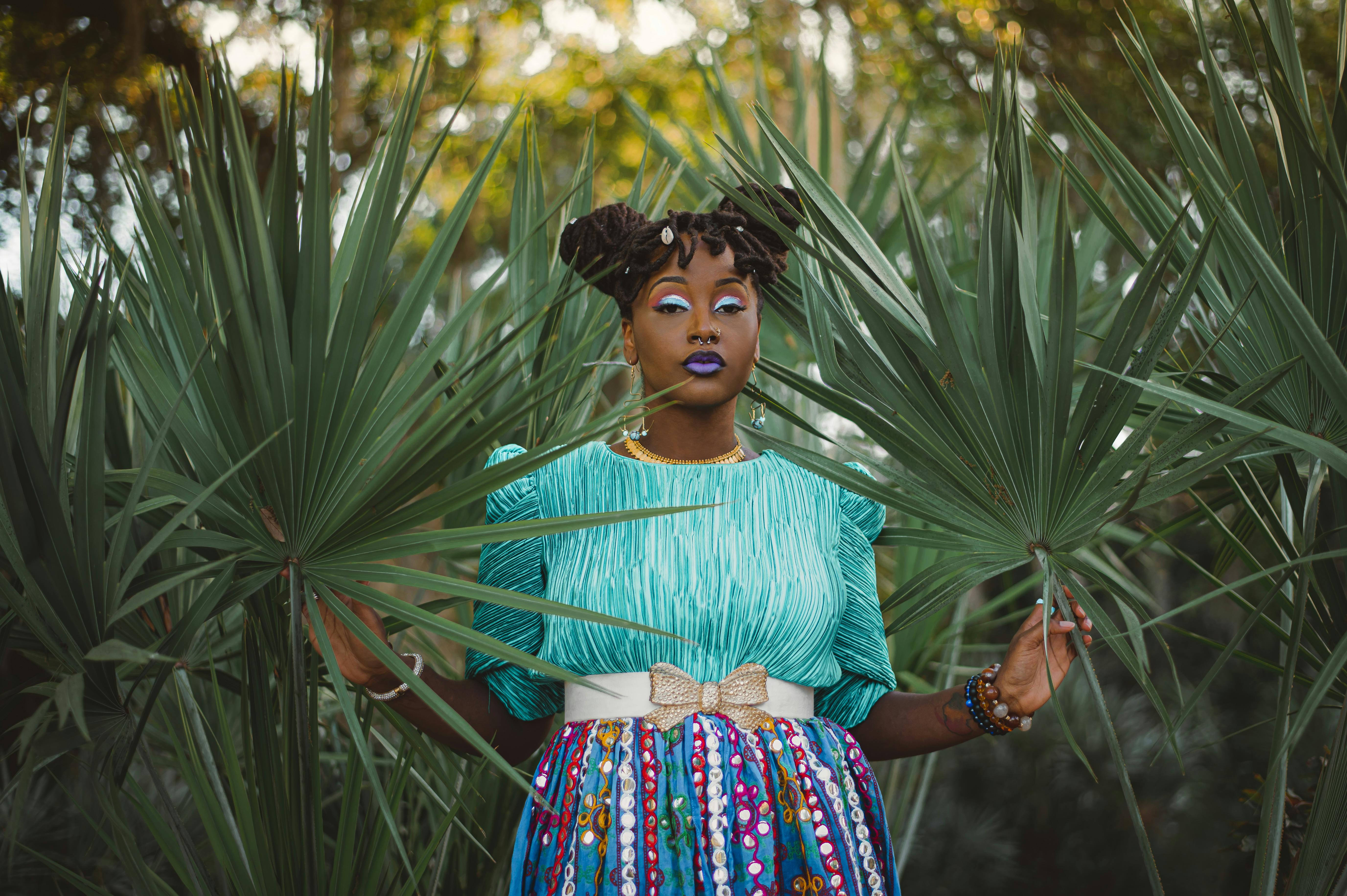 Vibrant portrait of a woman in colorful attire posing among fan palm leaves outdoors.