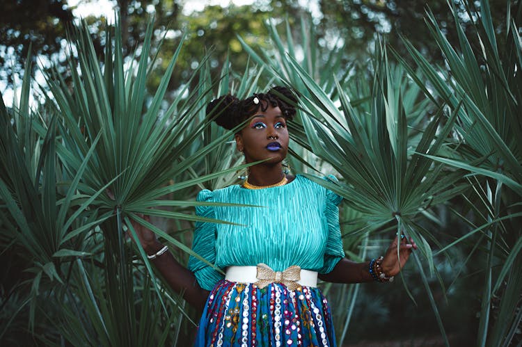 A Woman In A Blue Blouse And Multicolored Skirt Posing With Palmetto Leaves