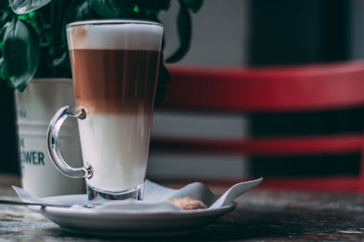 Close-up of a delicious layered latte in a glass, set on a rustic table with plant decor.