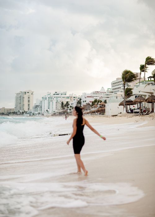 Free A woman in a black dress enjoys the beach in Cancún, Mexico, with resort buildings in the background. Stock Photo