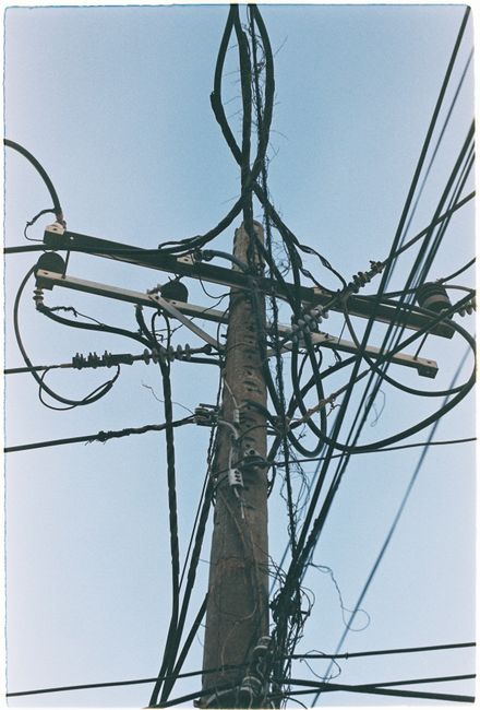 Photo by Nghia .8pm Complex web of utility wires on a wooden pole against a clear blue sky.