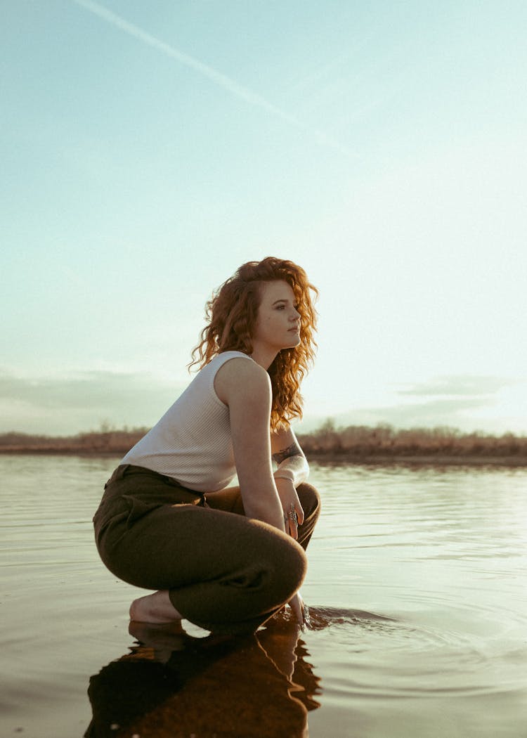 Woman With Curly Red Hair Crouching In Shallow Lake Water 