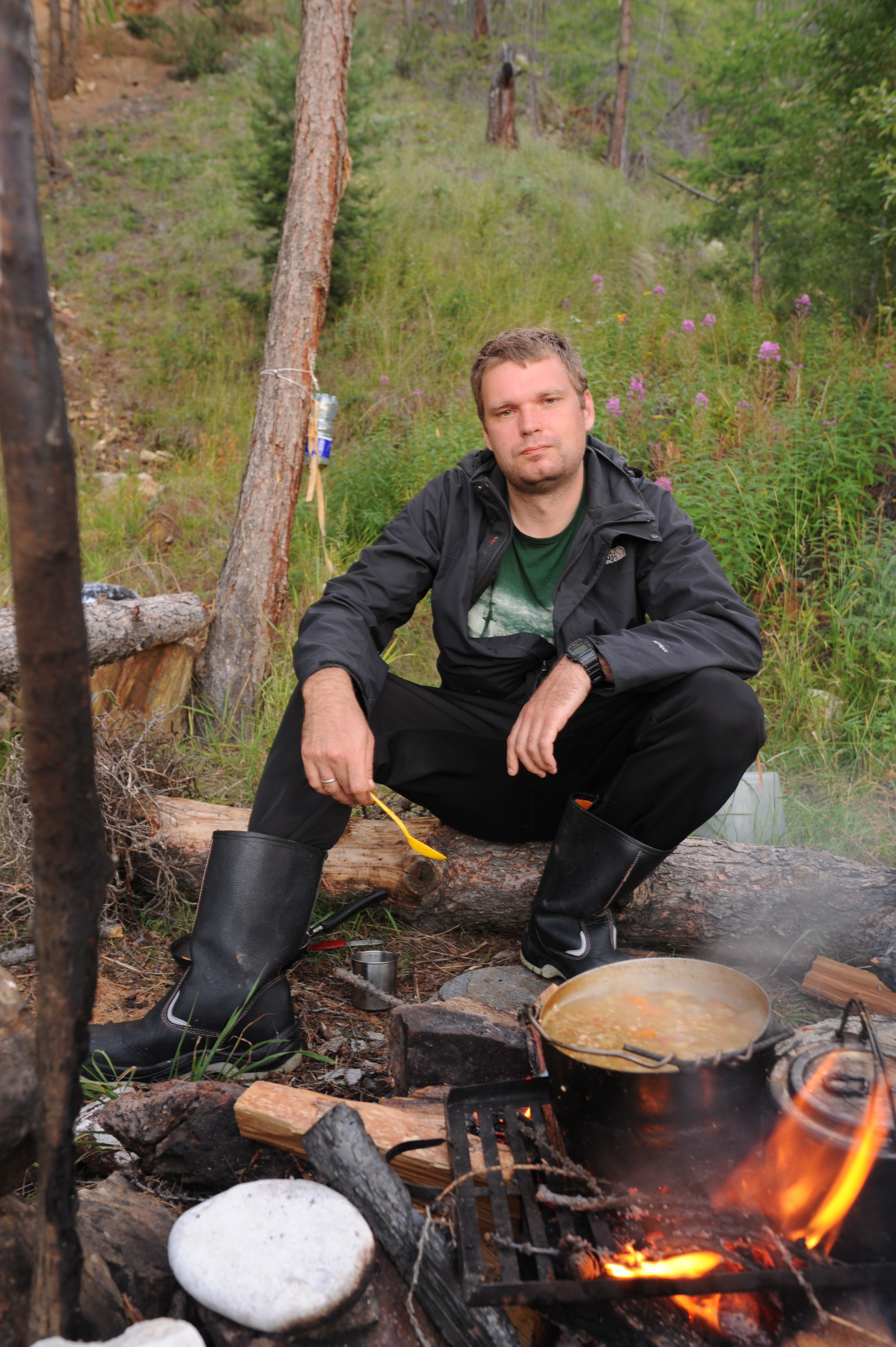 Outdoor scene with man cooking over campfire, surrounded by nature.
