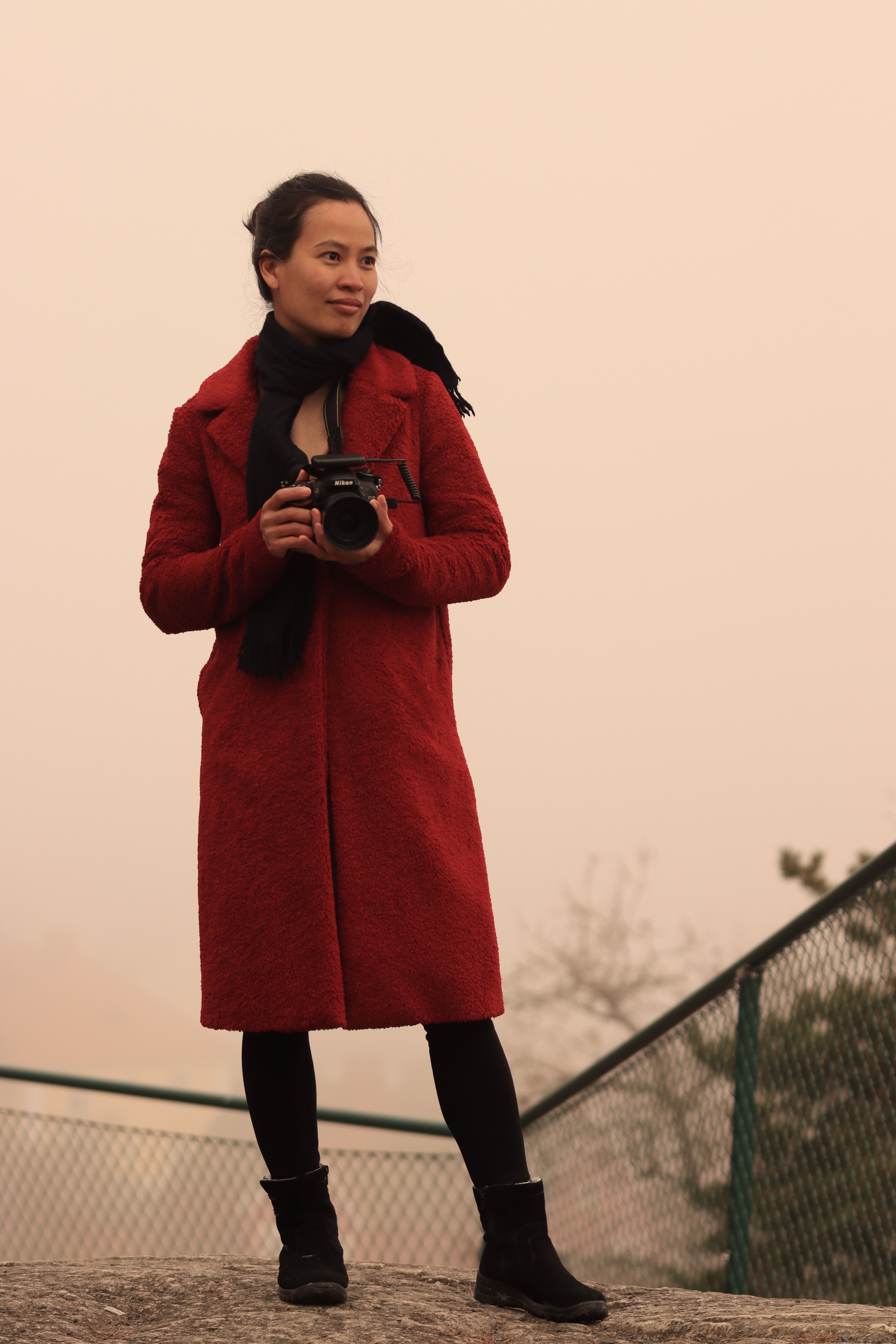 Asian woman in red coat holding camera outdoors in Jönköping, Sweden.
