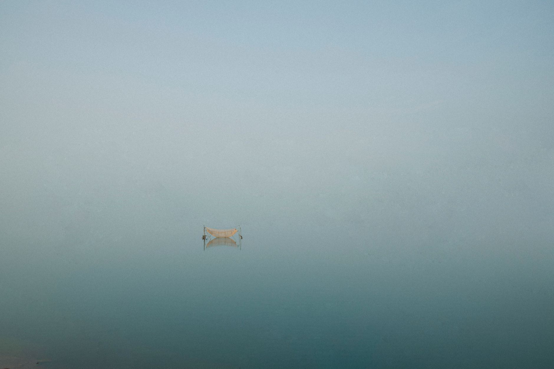 A solitary boat reflects on a tranquil, mist-covered lake in Gia Lai, Vietnam, capturing a serene and peaceful atmosphere.