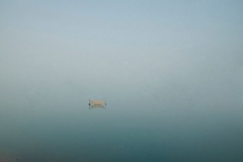 Free A solitary boat reflects on a tranquil, mist-covered lake in Gia Lai, Vietnam, capturing a serene and peaceful atmosphere. Stock Photo