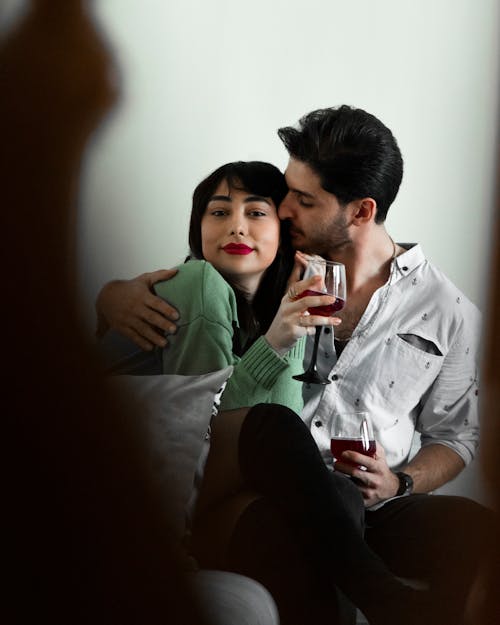 Free A Man Kissing Her Partner while Holding Wine Glasses Stock Photo