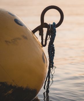 Close-up view of a buoy with a rusty hook and blue rope at sunset on calm water.