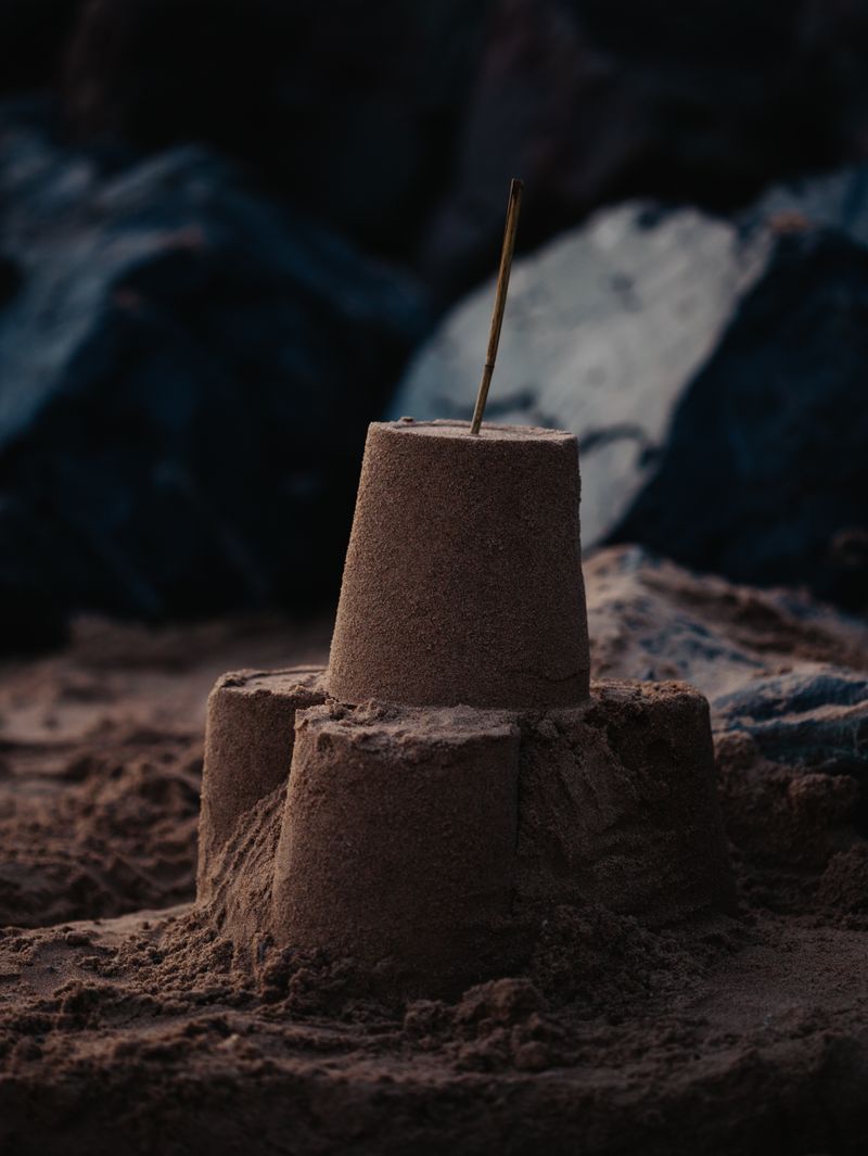 A sandcastle with a small flag on warm sand by the sea