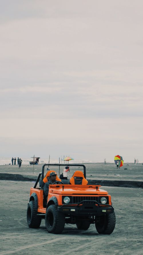 Free An orange Jeep driving on a beach in Indonesia under a cloudy sky, capturing a sense of adventure. Stock Photo