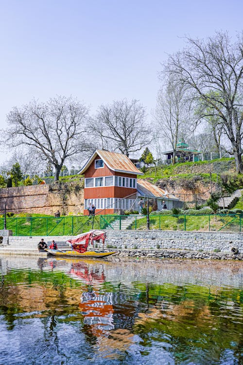People Riding on Boat on River Near Brown Wooden House