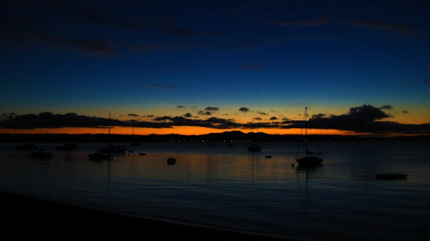 Beautiful sunrise over a calm lake with silhouetted boats and colorful sky.