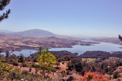 Free Stunning view of a serene mountain lake surrounded by lush greenery and hills under a clear blue sky. Stock Photo