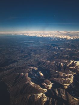 Stunning aerial view of vast, snow-capped mountain range stretching under a clear blue sky.