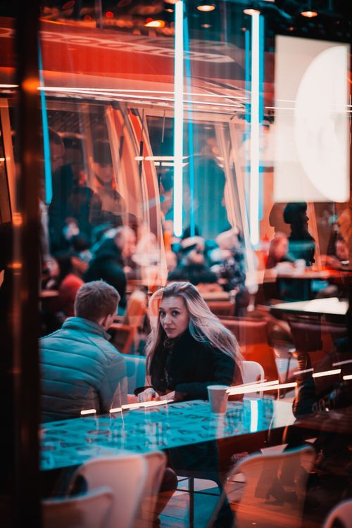 Free Cozy cafe atmosphere in Moscow, featuring a couple sitting behind glass with neon reflections. Stock Photo
