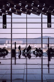 Silhouetted travelers in a modern airport terminal with large glass windows and waiting area.