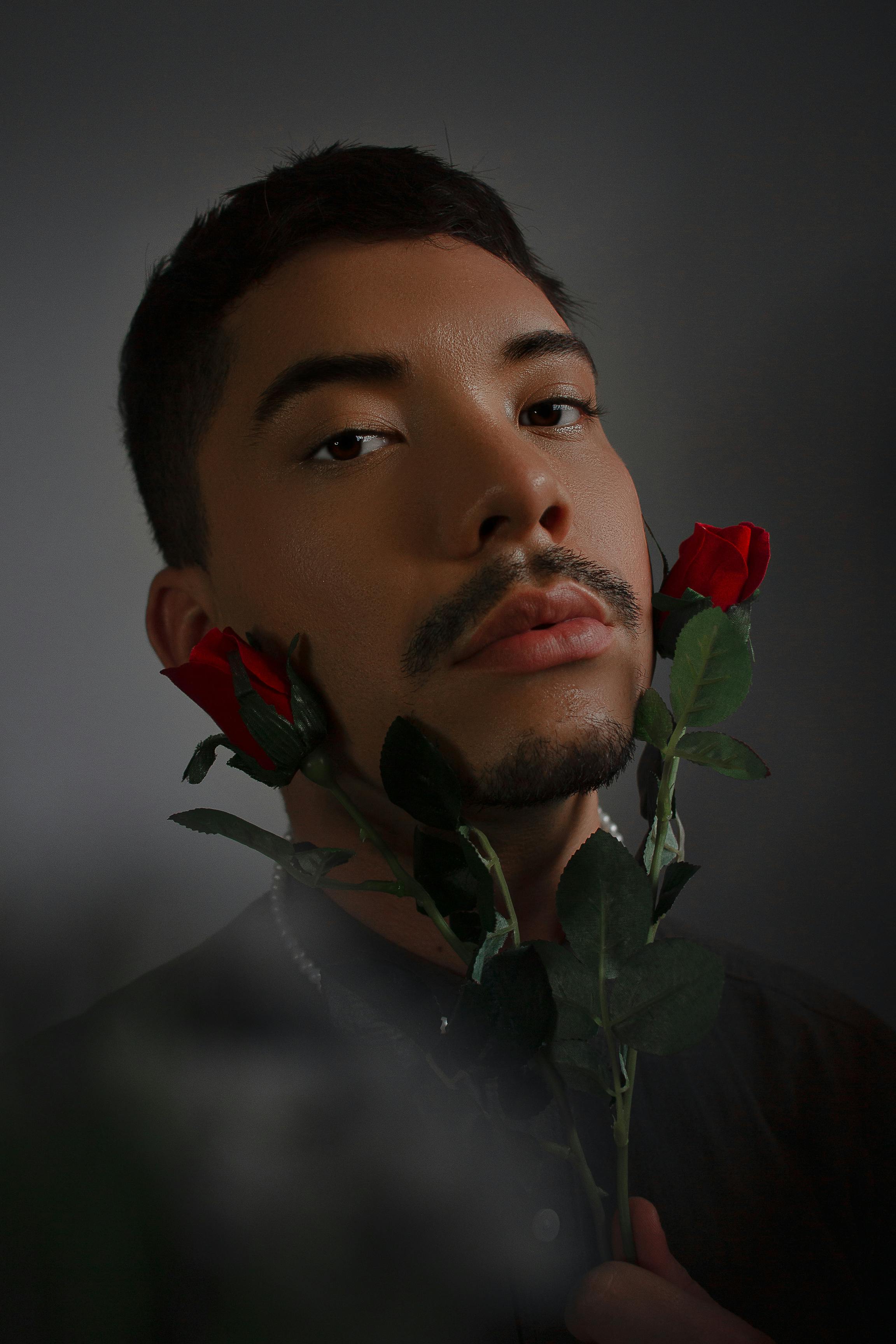 Close-up portrait of a man holding vibrant red roses, captured in a studio setting. Moody and artistic style.