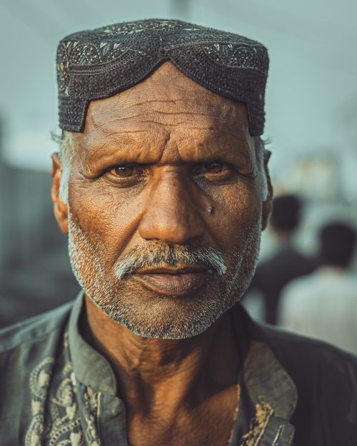 Free Close-up portrait of a senior man wearing a traditional hat outdoors, displaying wrinkles and a serious expression. Stock Photo