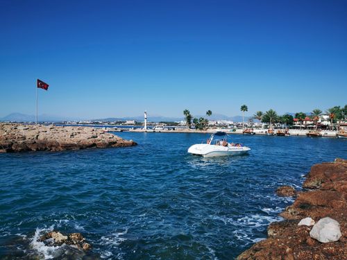 Free A tranquil boat ride near a rocky shoreline and harbor with clear blue skies and a Turkish flag. Stock Photo