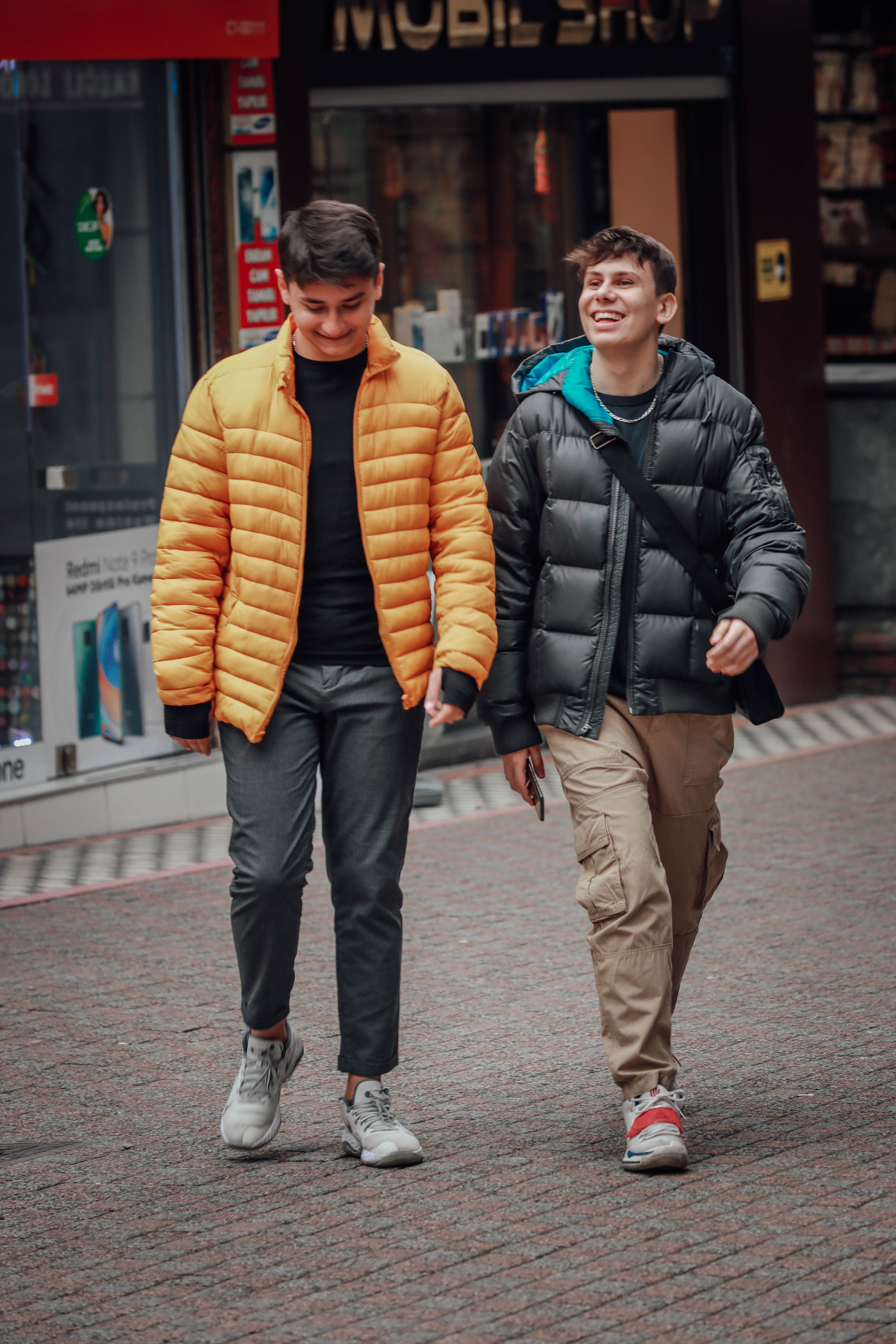 Two young adults walk casually in Ereğli, Türkiye, wearing winter jackets on a cobblestone street.