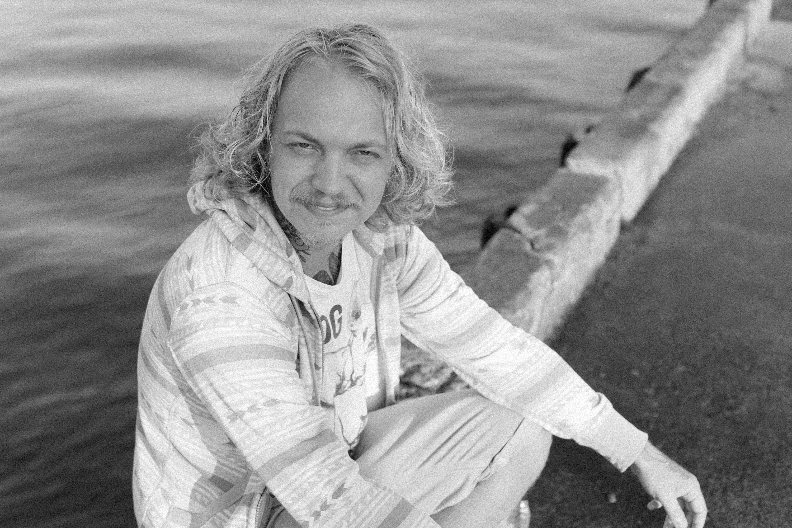 Grayscale photo of a man sitting by water's edge, exuding a serene mood.