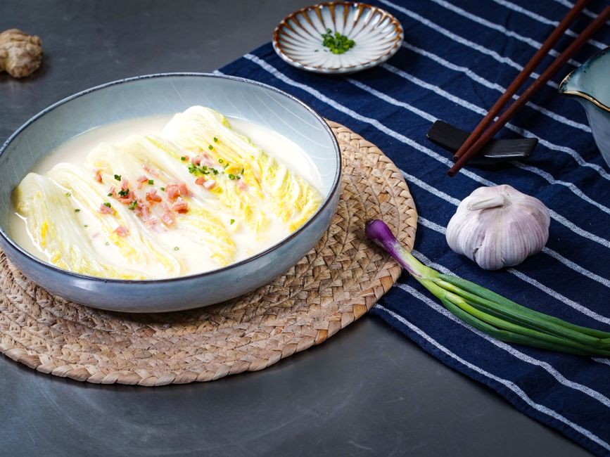 Traditional Asian cuisine featuring a cabbage dish in a creamy broth, garnished with garlic and chives.