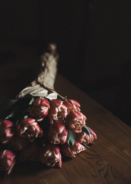 Free A close-up of a delicate bunch of pink tulips, artfully arranged on a wooden surface in dim lighting. Stock Photo