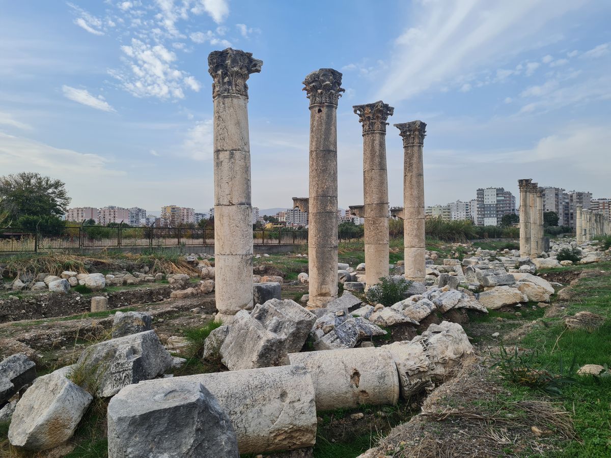 Excavated Roman-era column stumps fenced below street level, with the modern city skyline rising behind them.