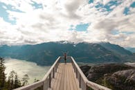 在史诗般的山景中，一个人在多云的天空下于木制平台上庆祝