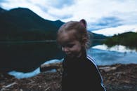 一个年轻的孩子坐在宁静的山湖边，背景是变幻的天空