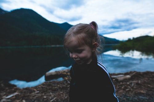 Free A young child by a serene mountain lake with a moody sky in the background. Stock Photo