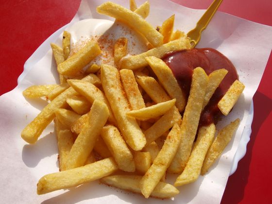 Golden fries dusted with paprika on a paper tray with ketchup, mayo and wooden fork