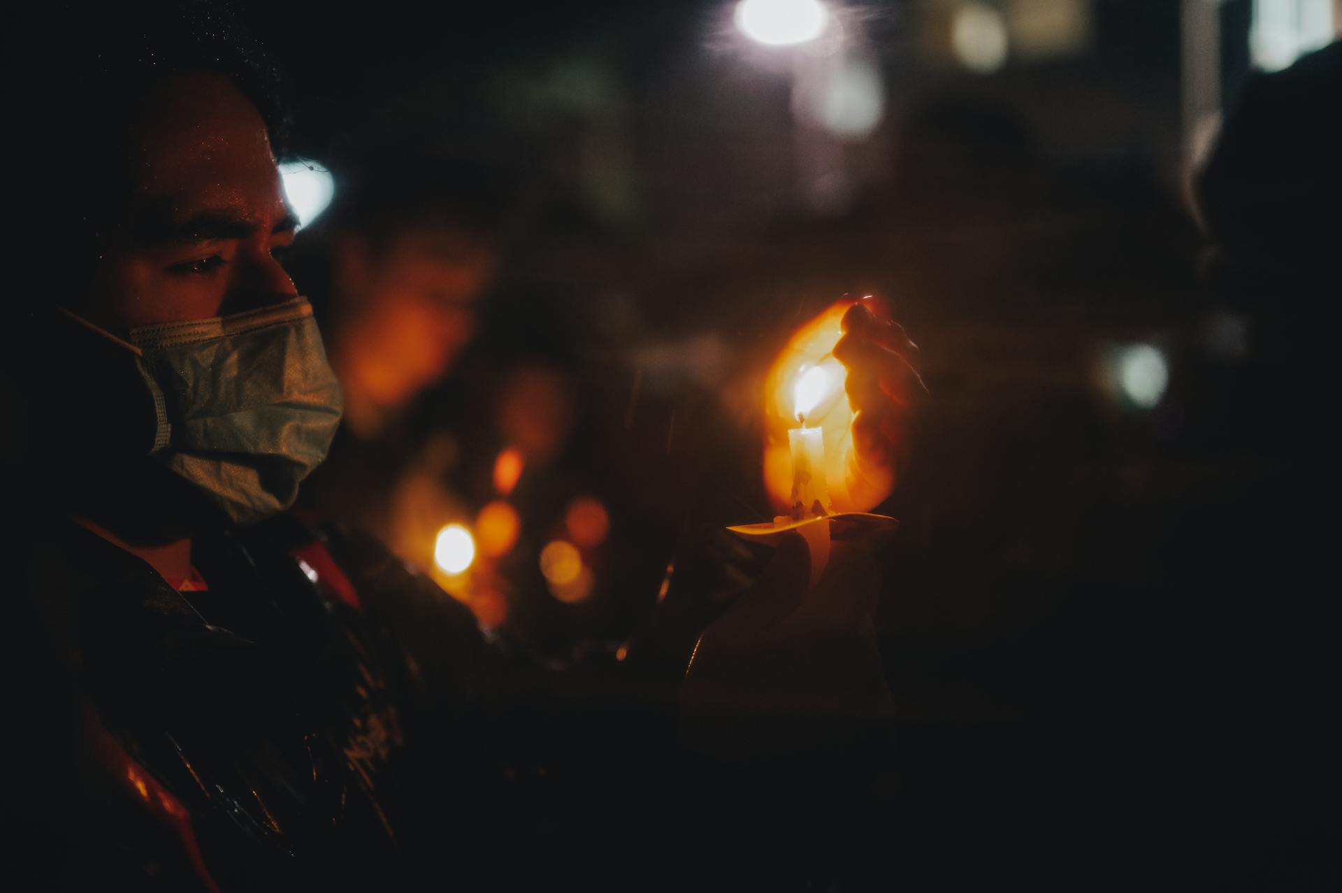 Person wearing a face mask holding a candle during a night vigil, symbolizing hope and resilience.