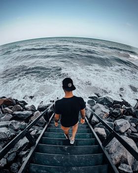Man in Black T-shirt and Brown Shorts Standing on Gray Staircase