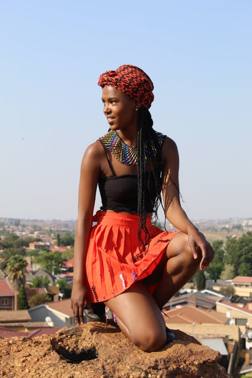 A Woman in Black Tank Top and Orange Skirt Sitting on the Rock while Looking Over Shoulder