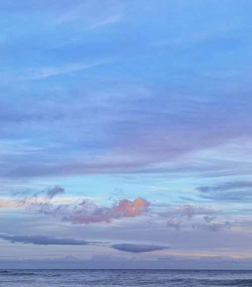 Free Tranquil seascape of the ocean meeting the blue sky with pastel clouds in Portimão, Portugal. Stock Photo