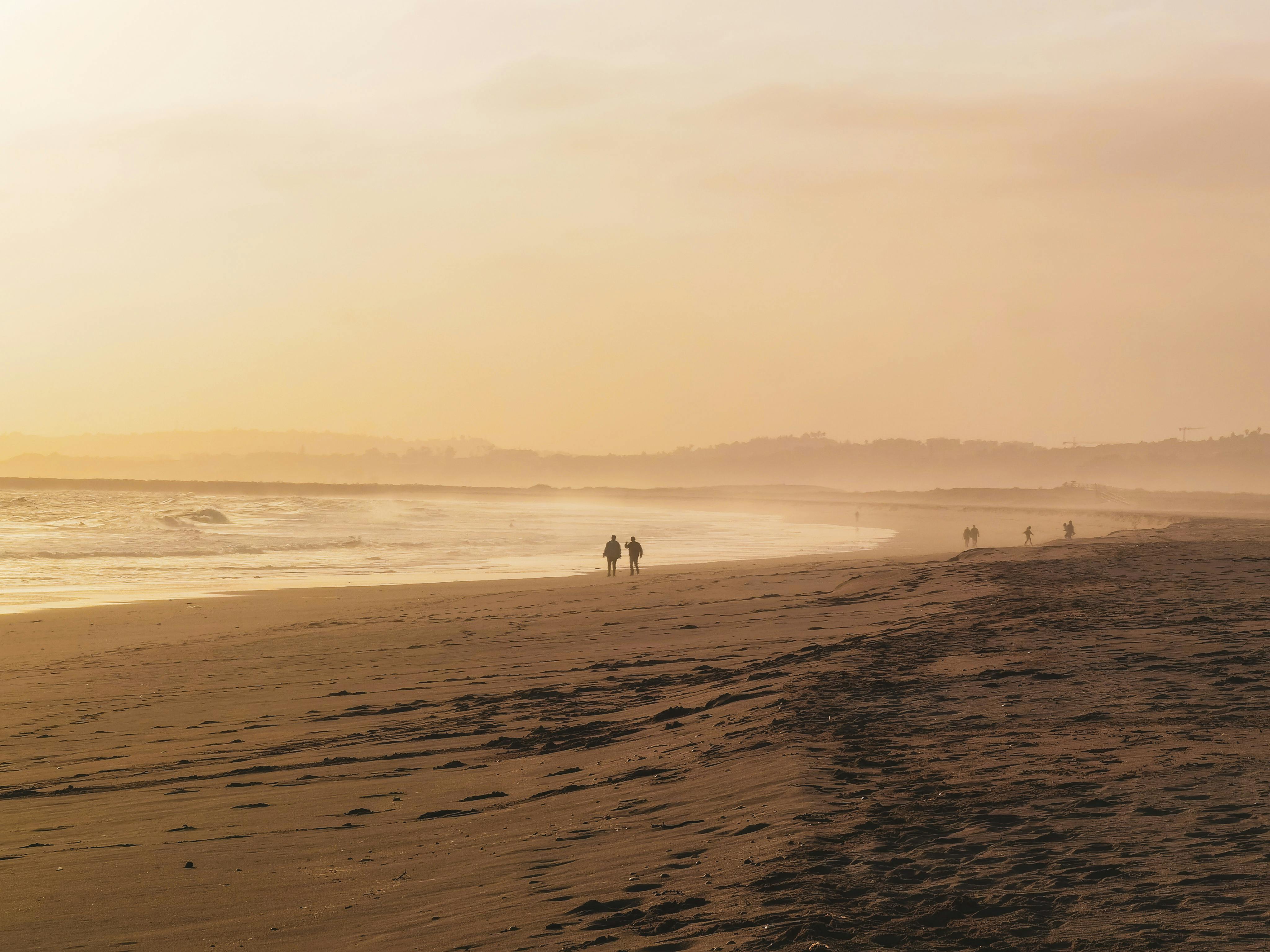 Two silhouettes walking on a sandy beach at sunset in Faro, Portugal with a golden sky.