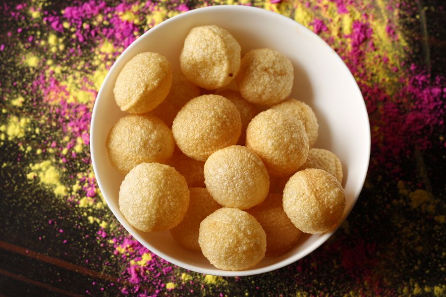 Top view of crispy Indian pani puri in a bowl with vibrant colored powder around.