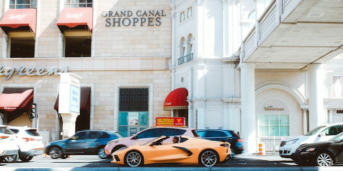 Vibrant view of luxury cars driving past Venetian Hotel in Las Vegas, highlighting urban vibrancy.