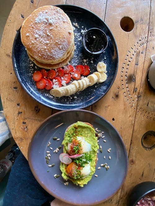 Avocado Toast and Stacks of Pancake with Strawberry and Banana Slices on Ceramic Plate