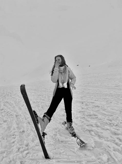 A Woman in Black Pants Standing on a Snow Covered Ground while Wearing Skis