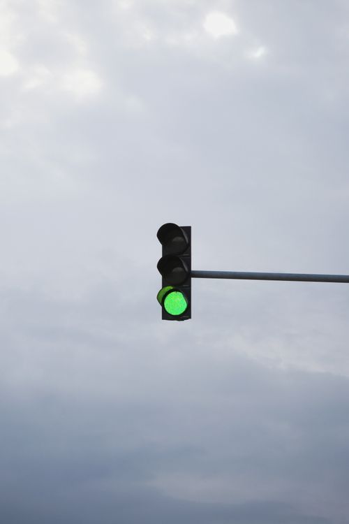 Free Green traffic light signaling go against an overcast sky, symbolizing forward movement. Stock Photo