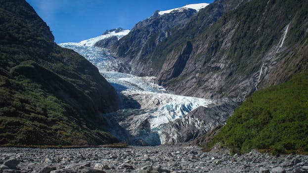 Captivating view of a glacier nestled between rugged mountain valleys under a clear blue sky.