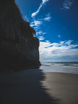Vertical shot of a beach with towering cliffs and a vivid blue sky, ideal for travel inspiration.