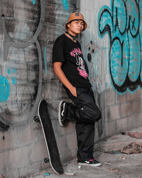 A Man in Black Shirt Leaning on a Concrete Wall while Wearing a Bucket Hat