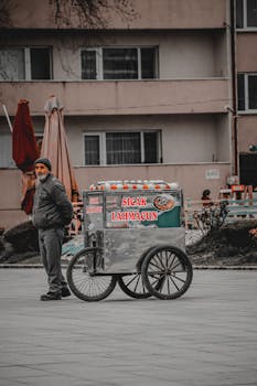 Mature street vendor standing with lahmacun cart outdoors in an urban area.