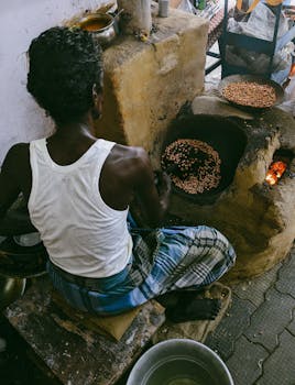 An adult male roasting peanuts on a rustic stove indoors, showcasing traditional cooking methods.