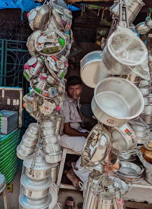 Free Man sitting among hanging kitchenware items at a street market stall. Stock Photo
