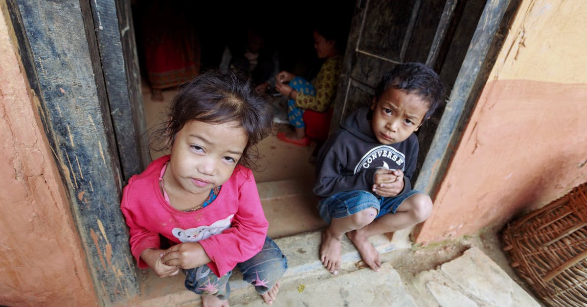 Curious children sitting in a doorway, looking up with inquisitive expressions.