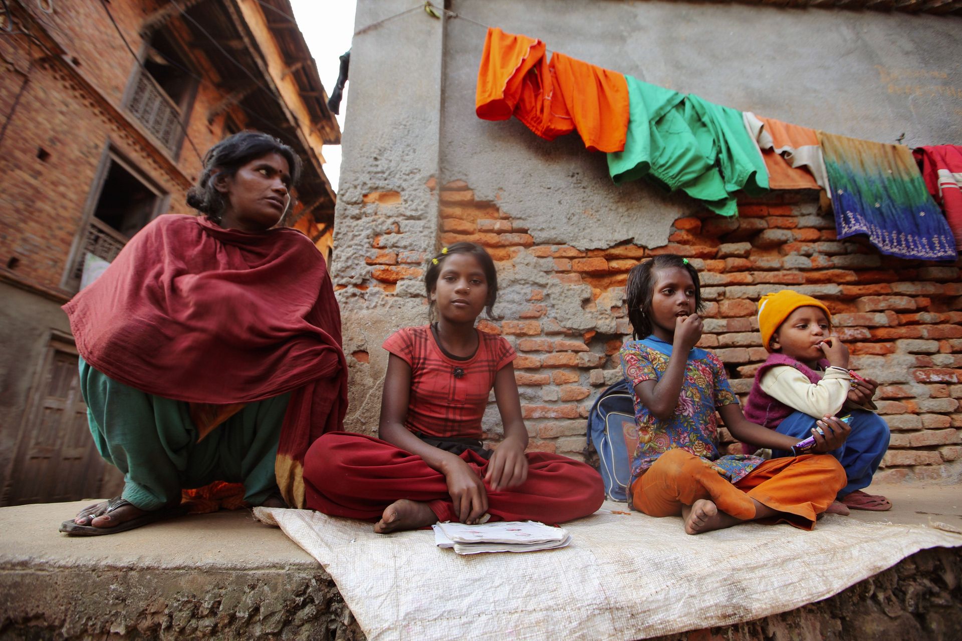 Family sitting against a brick wall in an urban neighborhood, showcasing vibrant clothing and a sense of community.